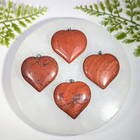 Four polished red jasper heart pendants with silver jump rings perfect for gemstone jewelry and crystal collections