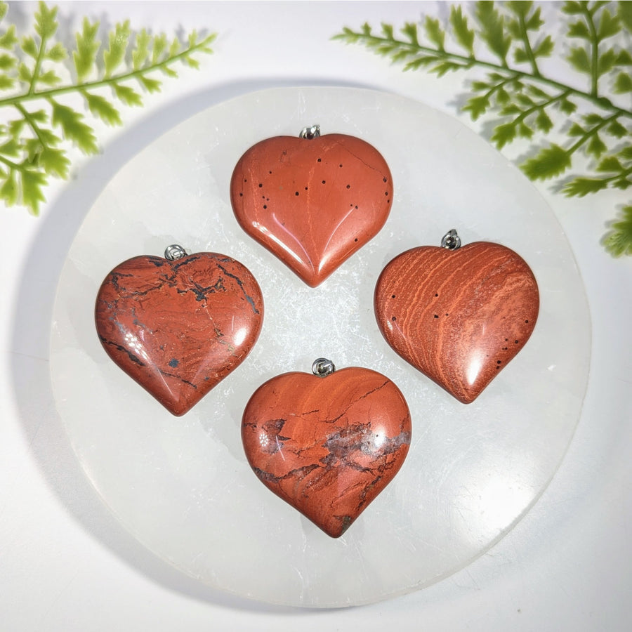 Four polished red jasper heart pendants with silver jump rings perfect for gemstone jewelry and crystal collections