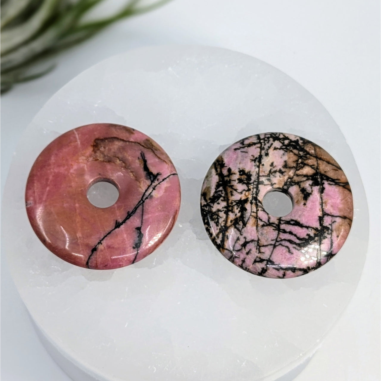 Two pink Rhodonite donut-shaped gemstone pendants with black veining patterns