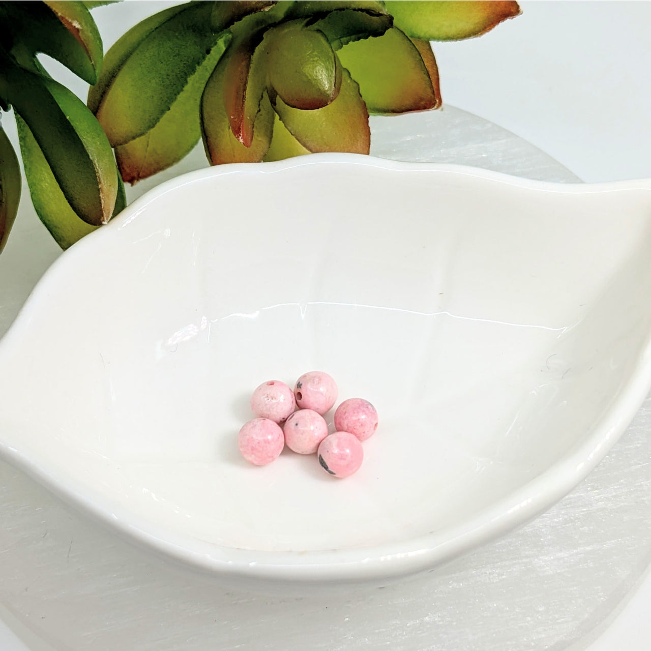 Pink pills in a white dish showcasing Rhodonite 6mm Round Beads Pack of 6 LV7156