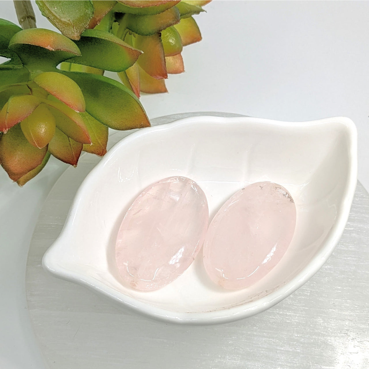 Two Rose Quartz 40mm flat oval beads in a white leaf-shaped dish