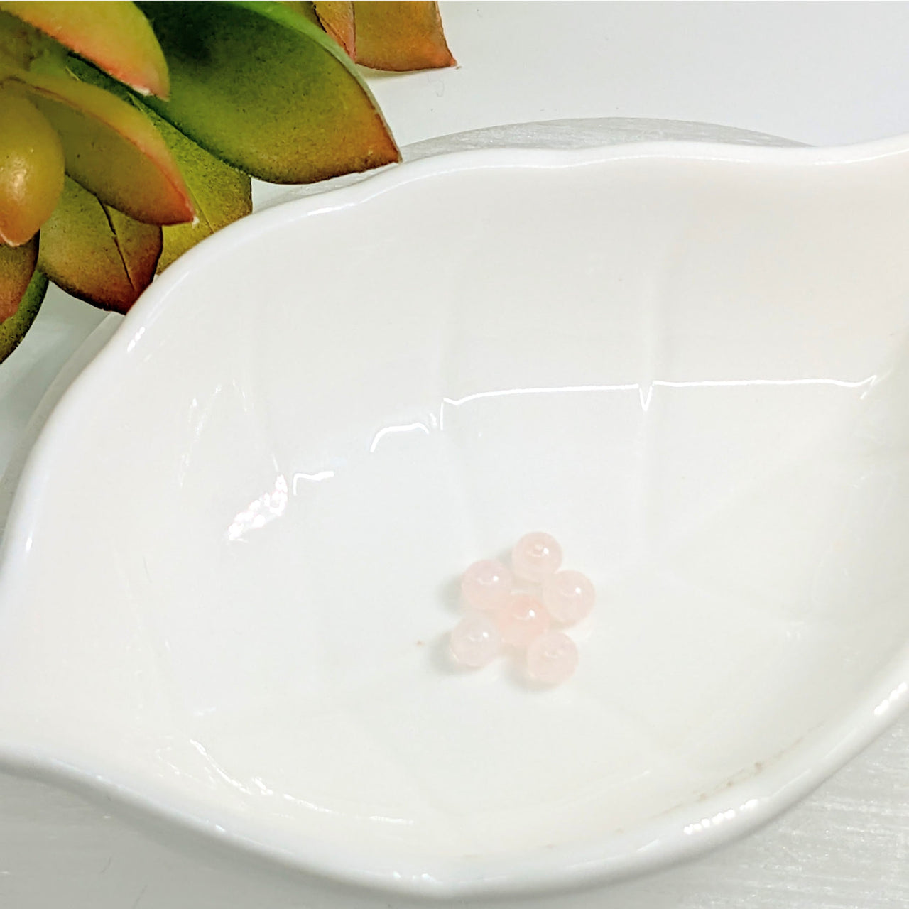 White ceramic spoon-shaped dish with pink flower design next to Rose Quartz 4mm Mini Round Beads