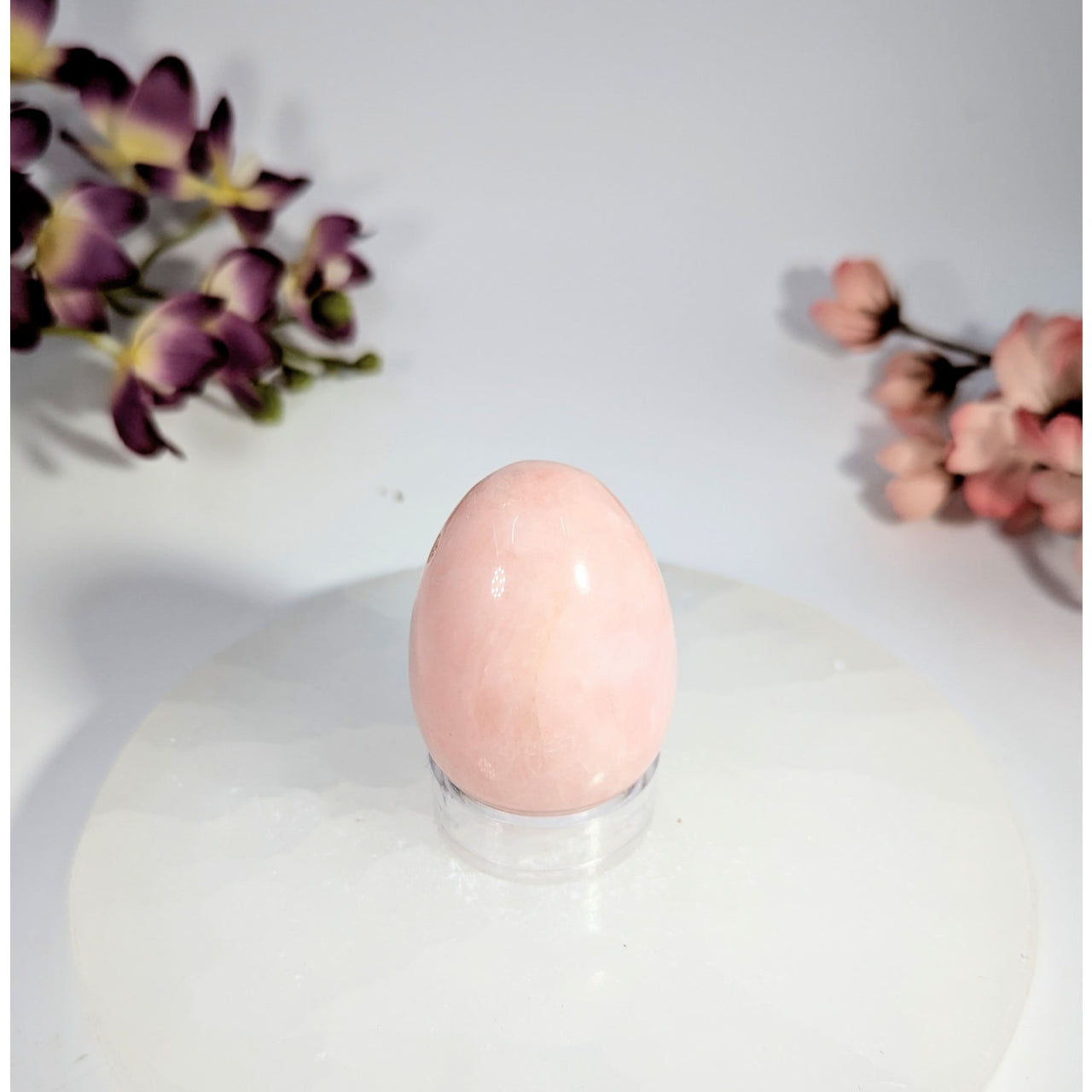 Smooth pale pink rose quartz yoni egg with hole on acrylic stand