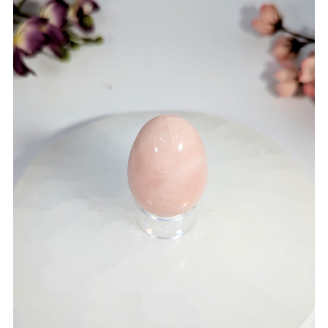 Smooth pale pink rose quartz yoni egg with hole on clear stand