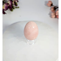 Smooth pale pink rose quartz yoni egg with hole on clear stand