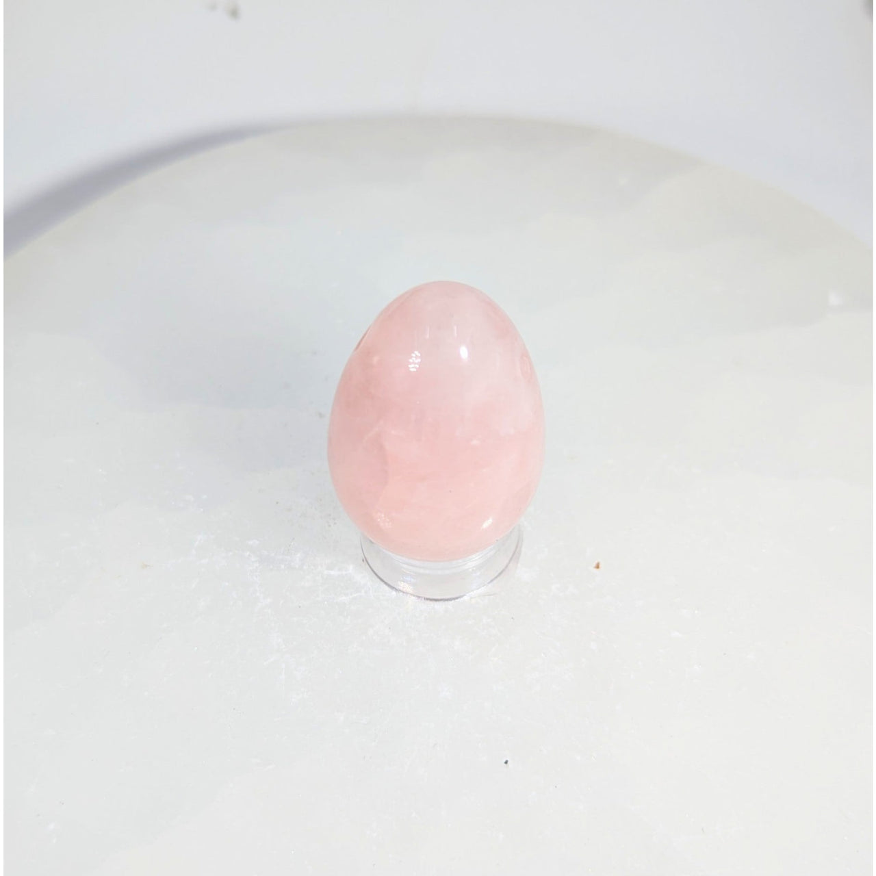 Smooth translucent pink rose quartz yoni egg with hole on acrylic stand
