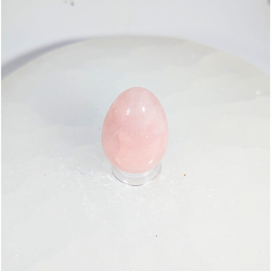 Smooth translucent pink rose quartz yoni egg with hole on acrylic stand