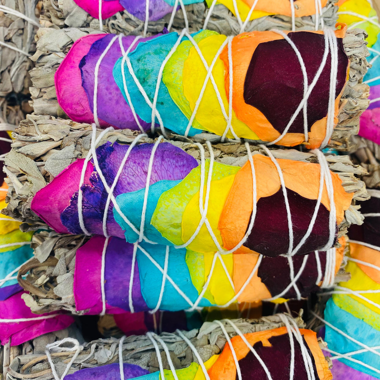 Rainbow-colored sage bundle featuring blue sage smudge sticks tied with white string