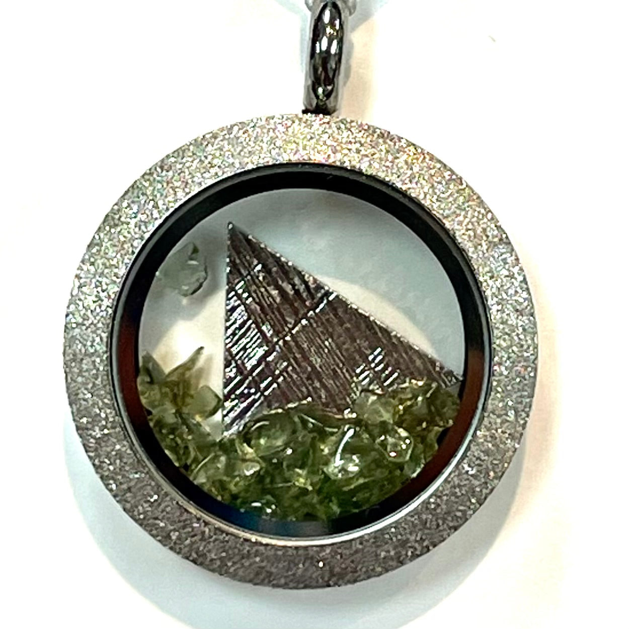 Silver phenacite locket pendant with green crystals and metallic triangle behind glass