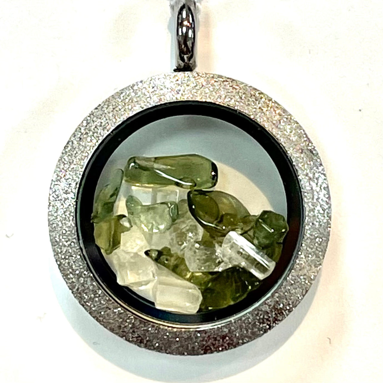 Round silver Phenacite locket pendant with green and clear crystals behind glass