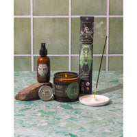 Lit burning amber glass candle with green Sea Witch Botanicals fairy label