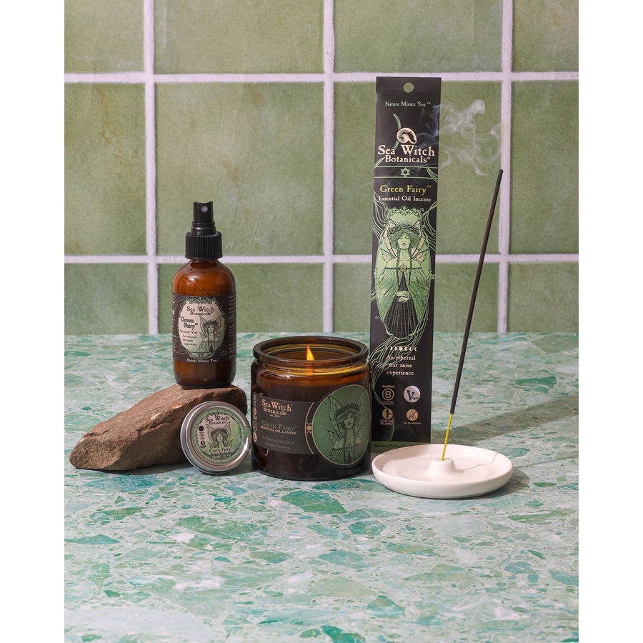 Lit burning amber glass candle with green Sea Witch Botanicals fairy label