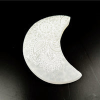 White crescent-shaped Gua Sha tool with intricate engraved floral patterns on Selenite Moon Plate