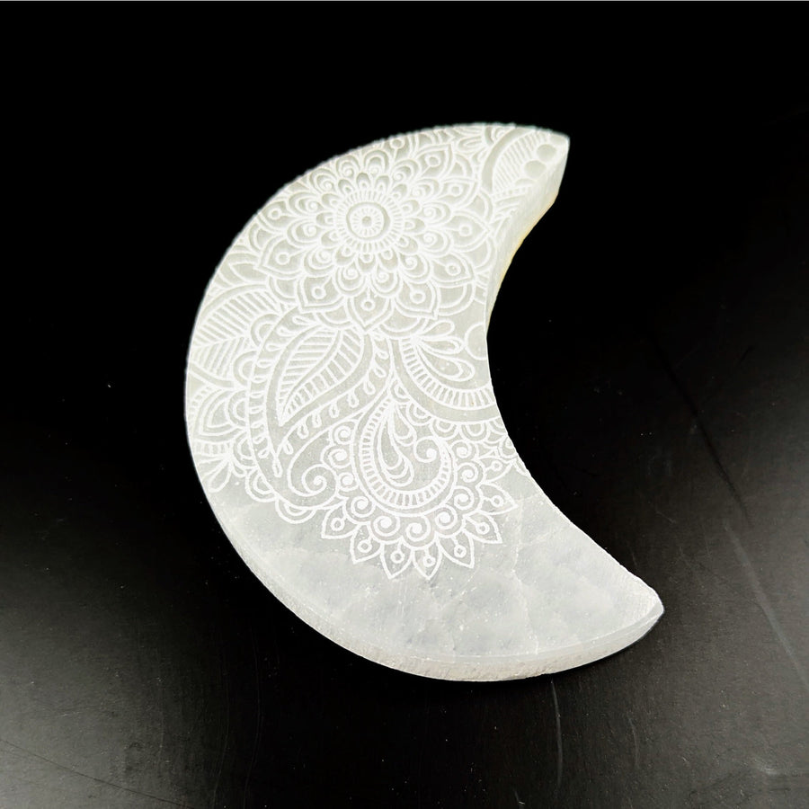 White crescent-shaped Gua Sha tool with intricate engraved floral patterns on Selenite Moon Plate