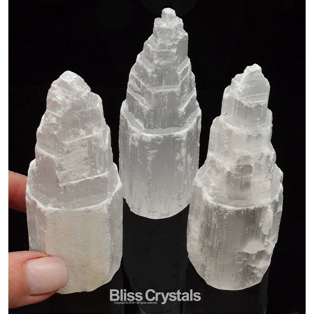 Hand holding white quartz crystal with two more beside the SELENITE Skyscraper Tower