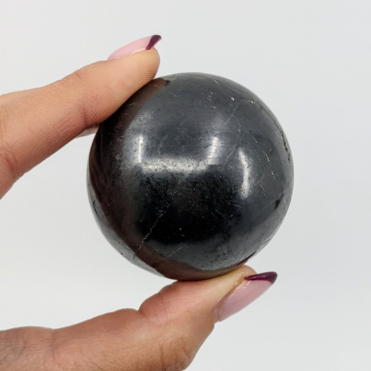 Hand holding Shungite 1.9’ Sphere (140g) - Black Marble Ball #SK9328 for Healing and Meditation