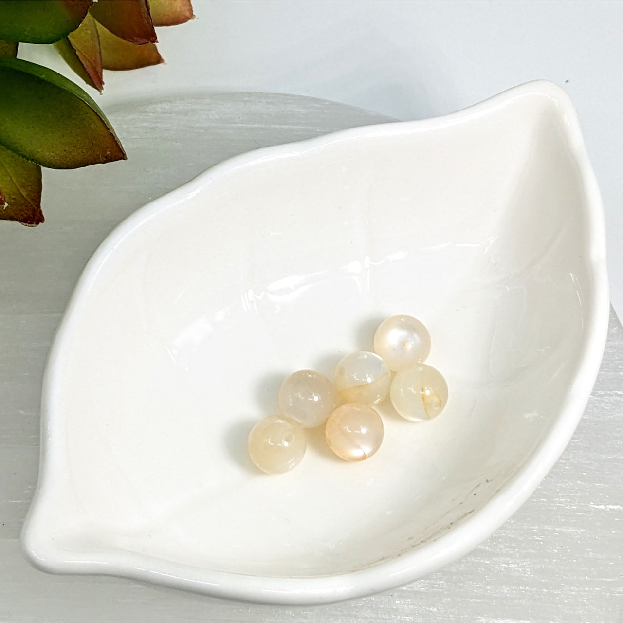 White leaf-shaped ceramic dish with Silver Moonstone 8mm round beads displayed