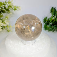 Smoky quartz 2.1 inch sphere with translucent smoky quartz and golden inclusions on a white geometric-patterned stand