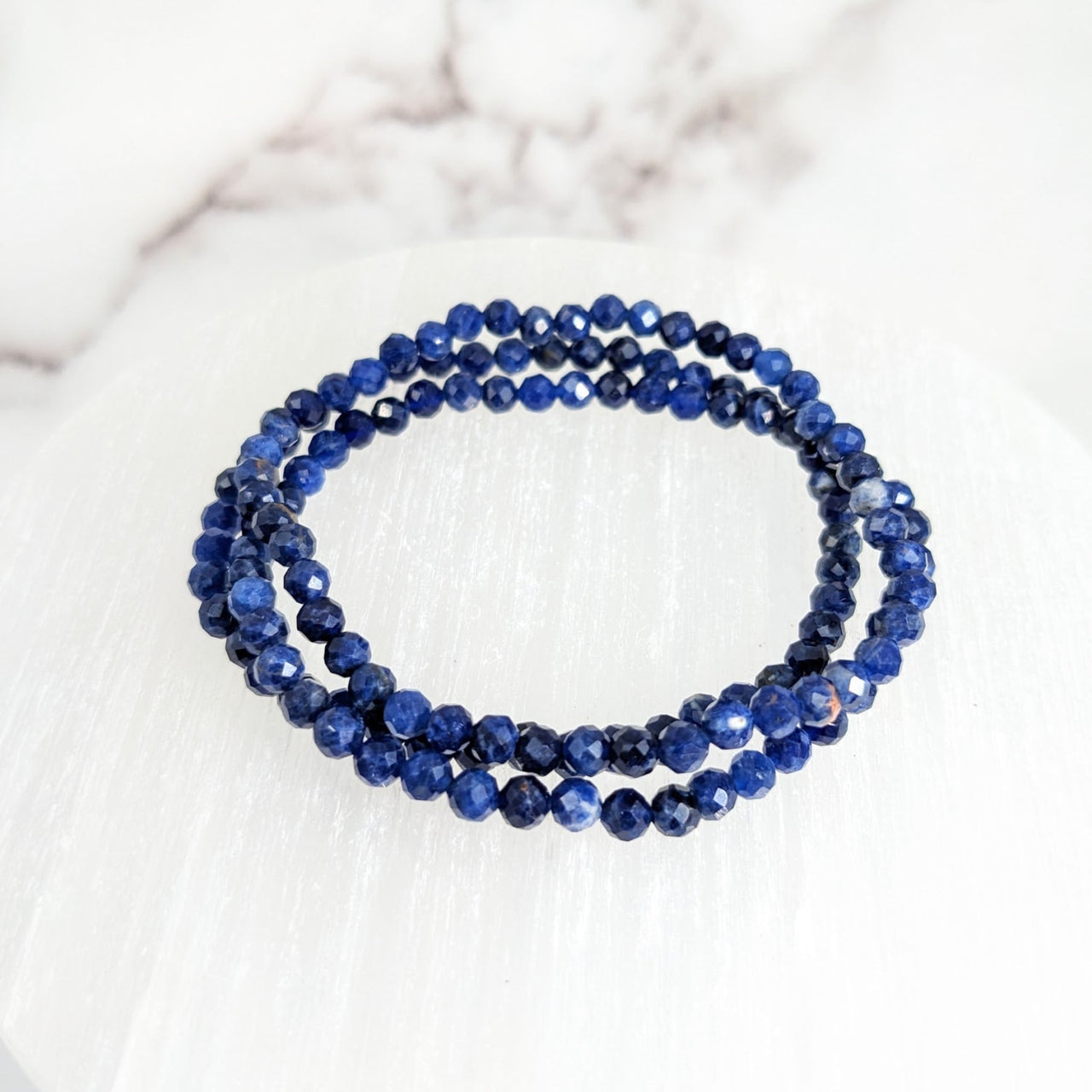 Close-up of Sodalite Faceted 7’ 4mm Bead Bracelet #LV2149 with blue beads on a marble surface