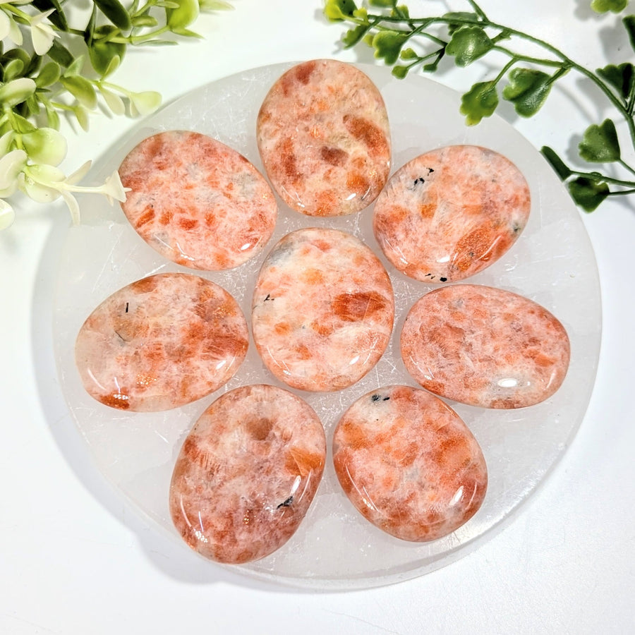 Seven polished orange and white sunstone palm stones arranged in a circle on a clear crystal plate