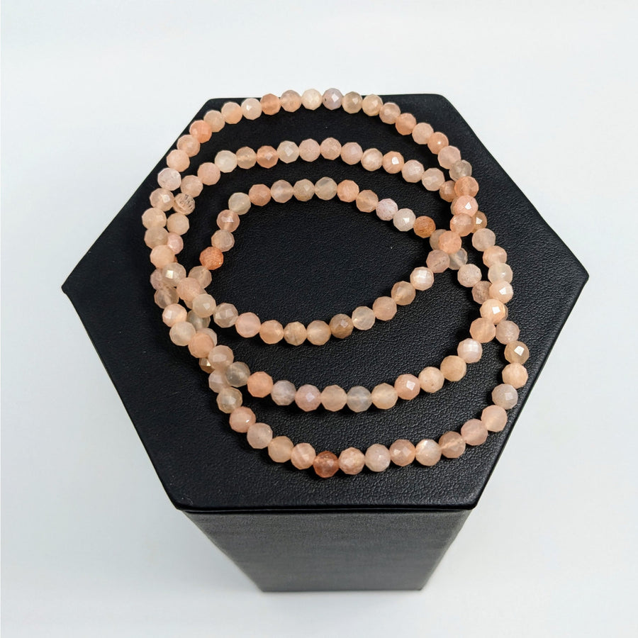 Peach-colored beaded Sunstone bracelet coiled on a black hexagonal surface
