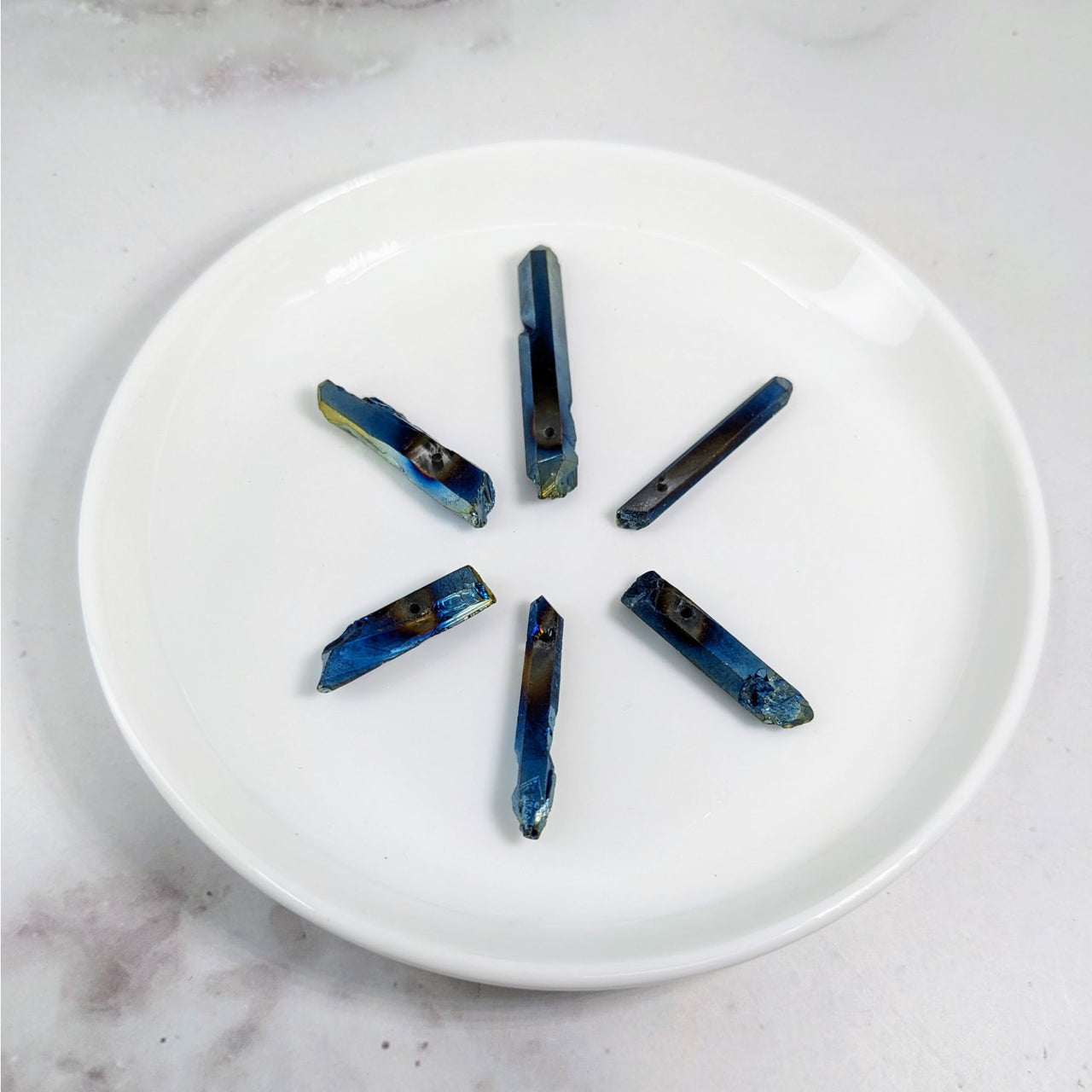 Titanium Aura 6 Pack Quartz Point Drilled Bead #LV3606 on a White Plate with Blue and Yellow Beads