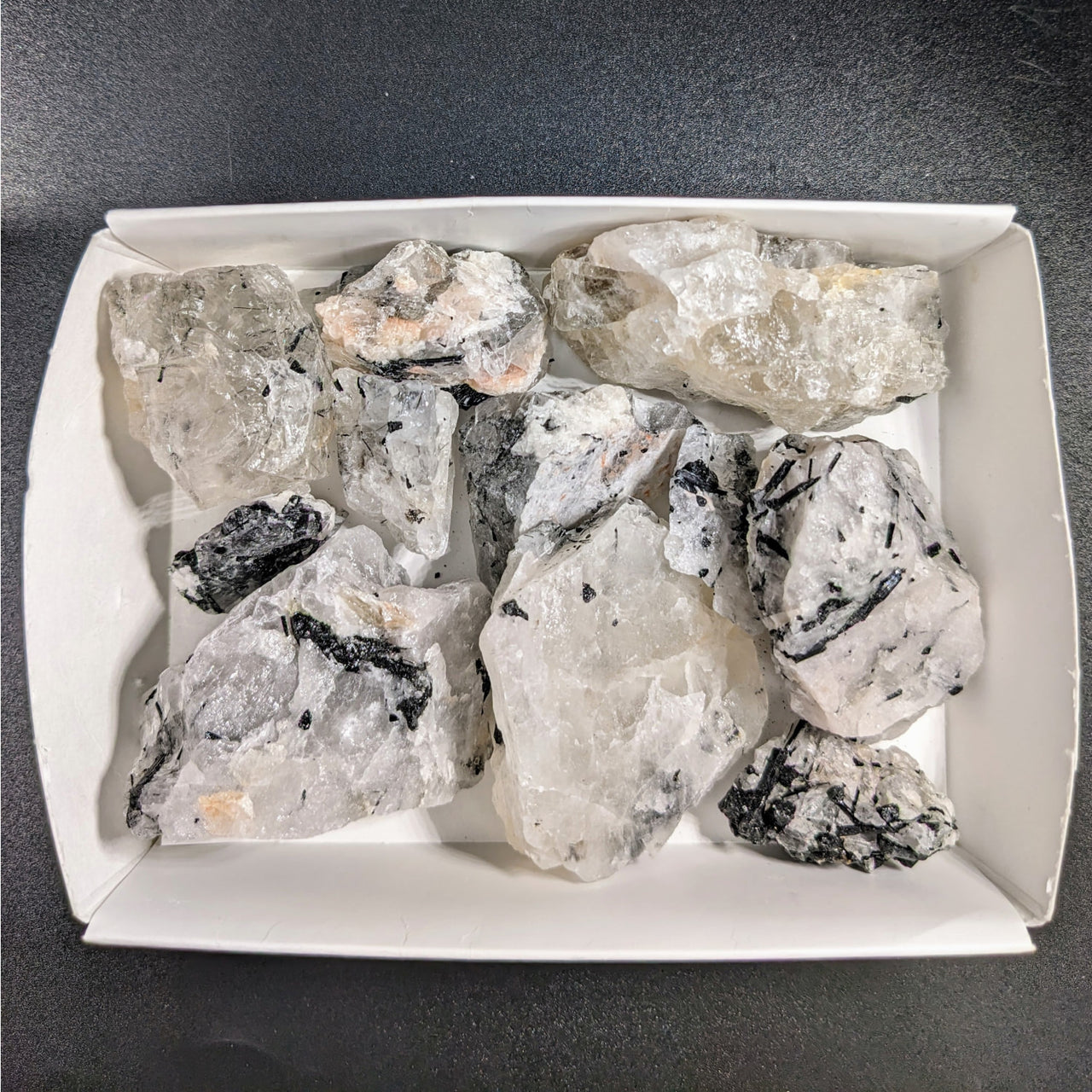 A white plate with ice and mixed sizes of rough tourmalinated quartz pieces