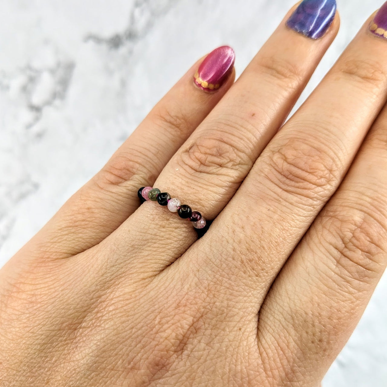 Woman’s hand wearing Tourmaline Mixed Beaded Stretchy Ring #LV1970 in purple and black