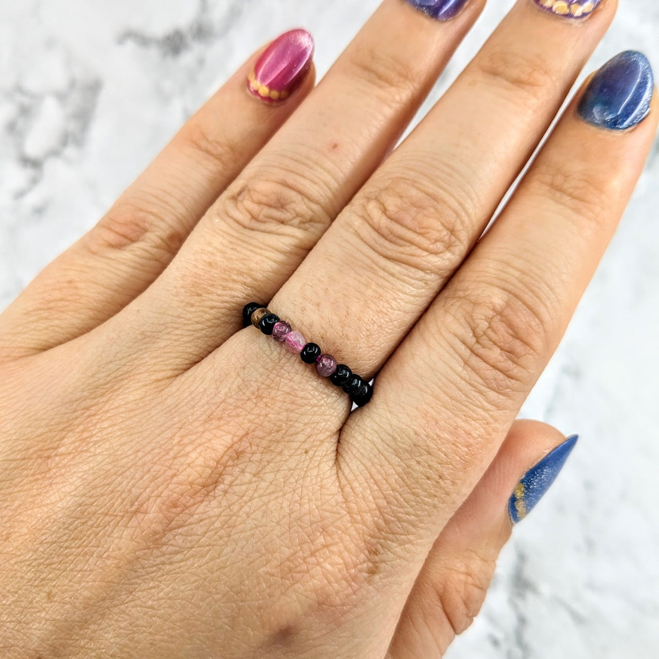 Tourmaline Mixed 1’ Beaded Stretchy Ring #LV1970 on a woman’s hand with purple and black design
