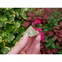 A translucent green vesuvianite pyramid crystal 0.75 inch held in a hand for metaphysical use