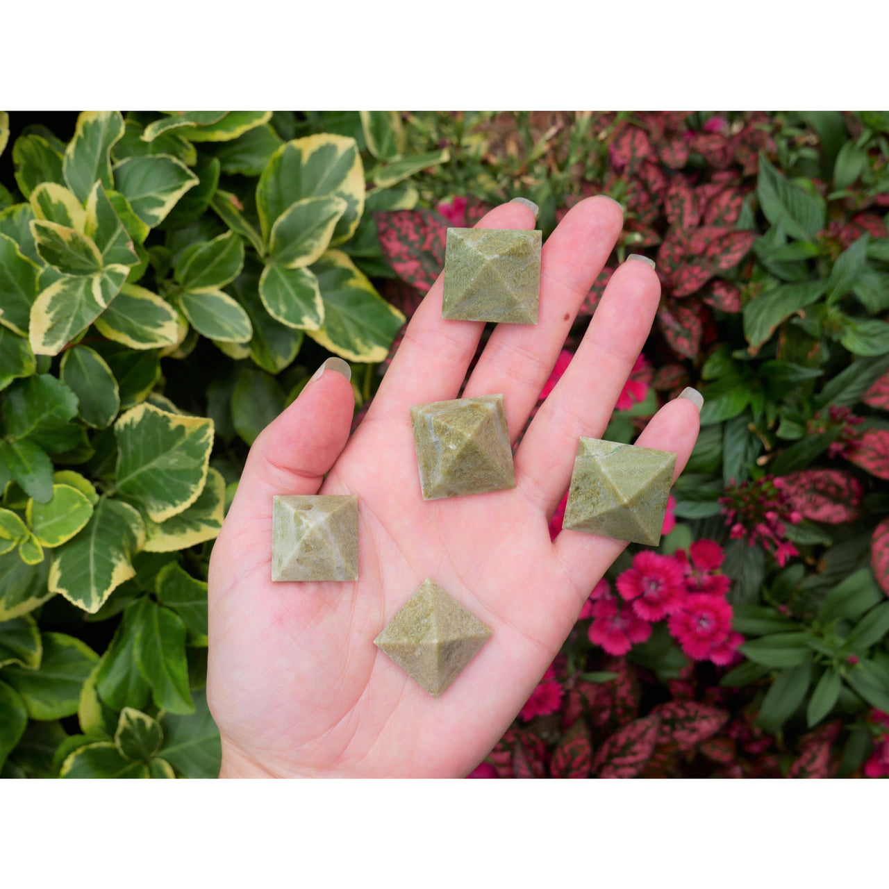 A hand holds five small matte green vesuvianite pyramids measuring 0.75 inches with a textured surface