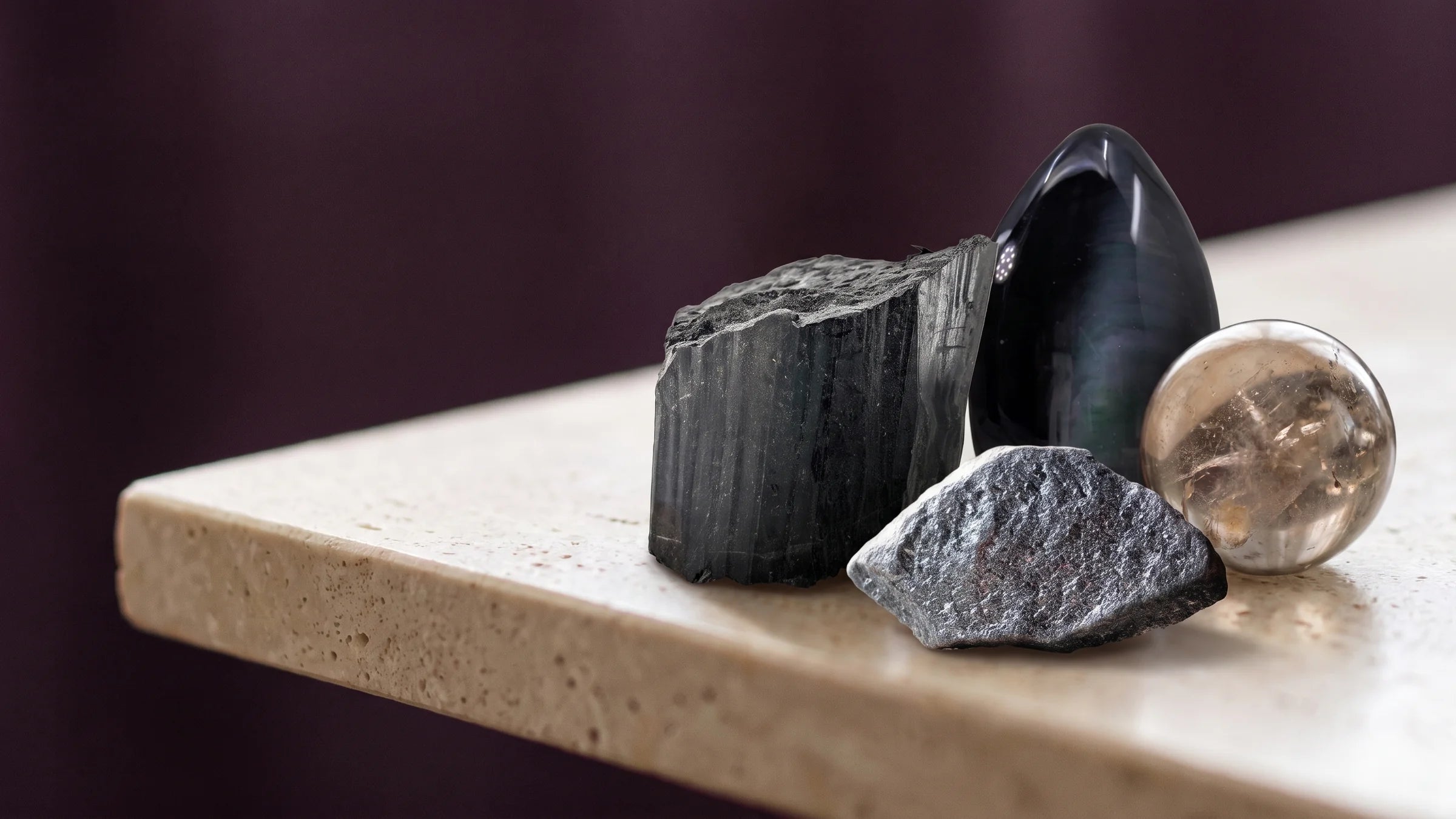 Black tourmaline, obsidian, hematite and smoky quartz grouped on a dark surface.