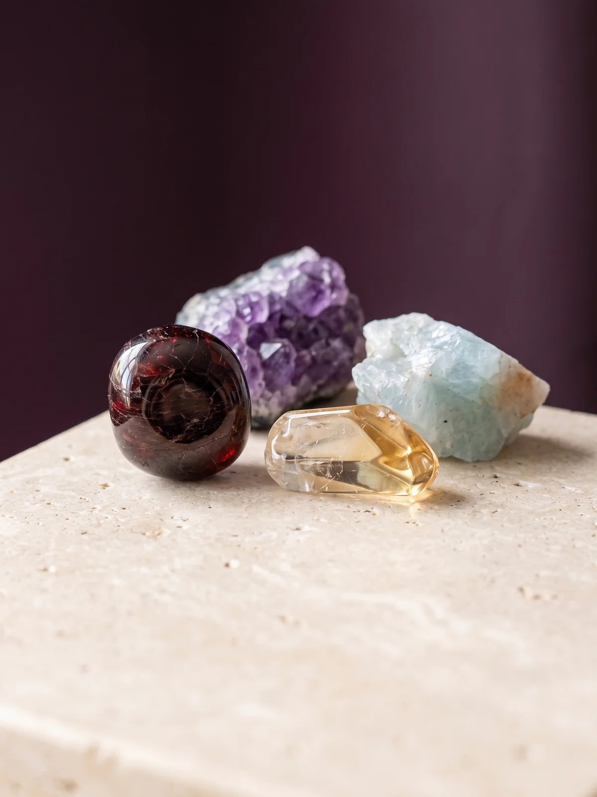 Garnet, amethyst, aquamarine and citrine birthstones grouped on warm travertine.