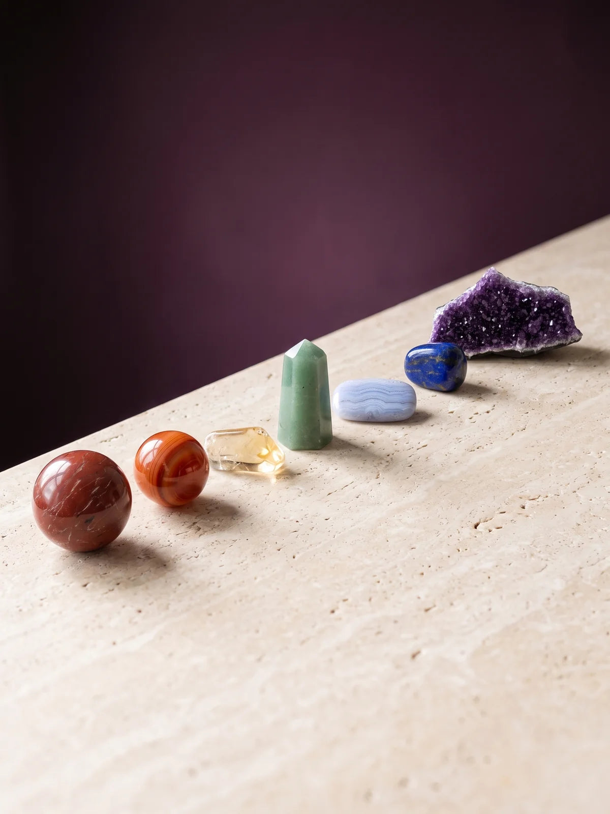 Seven chakra-associated crystals in a gentle diagonal line, root to crown.