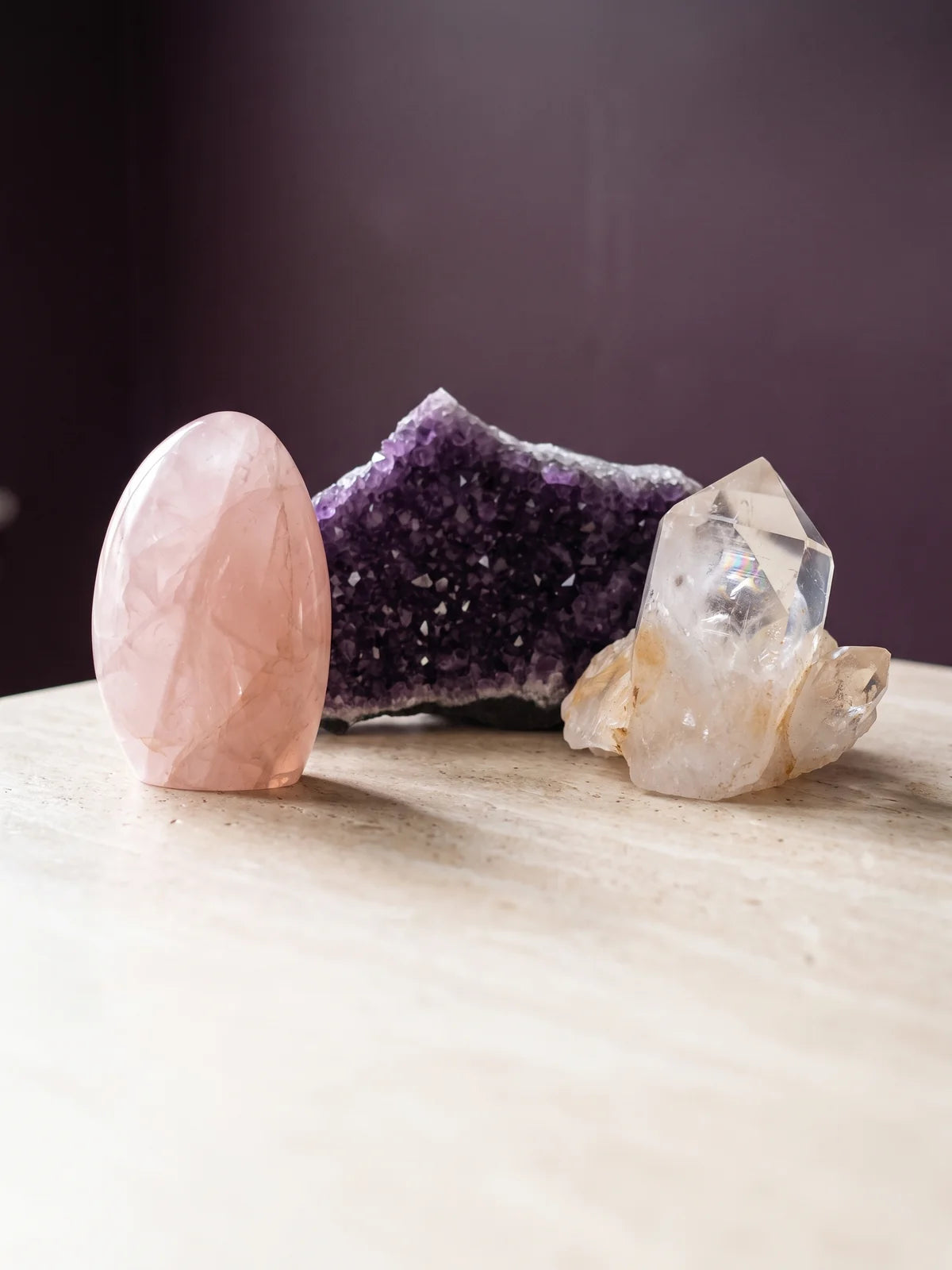 Rose quartz, amethyst and clear quartz specimens grouped on warm travertine.
