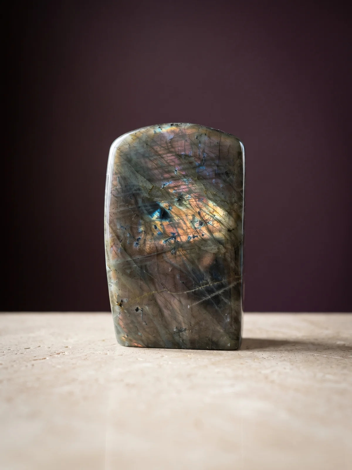 A labradorite specimen with blue-green flash against a deep plum backdrop.