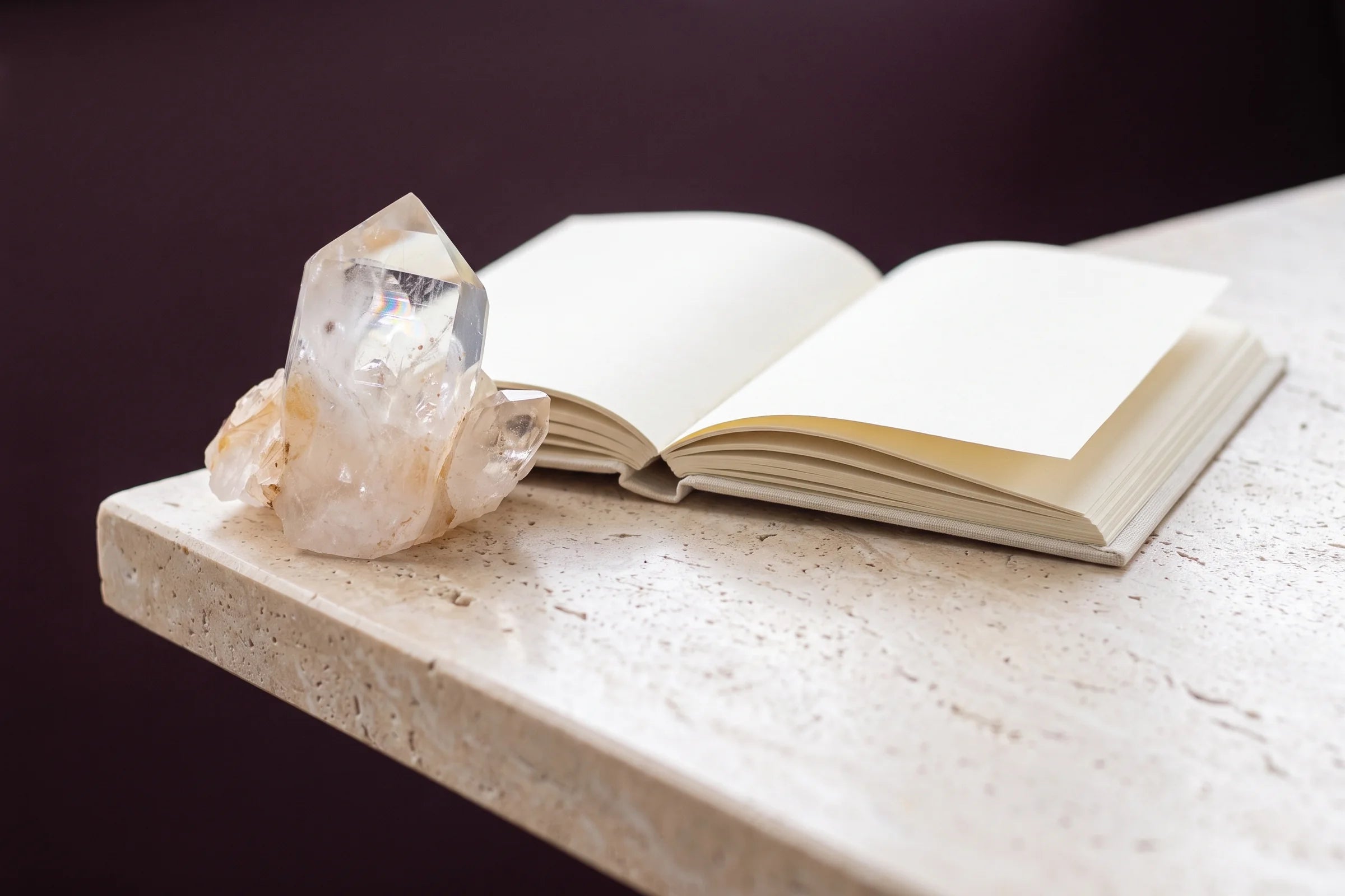 An open journal beside a clear quartz specimen on warm travertine.